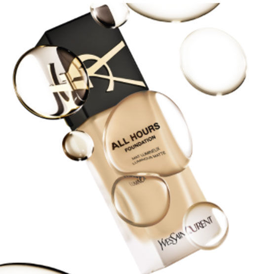 A bottle of Yves Saint Laurent All Hours Foundation surrounded by bubbles, showcasing a light beige shade and emphasizing a sleek design.