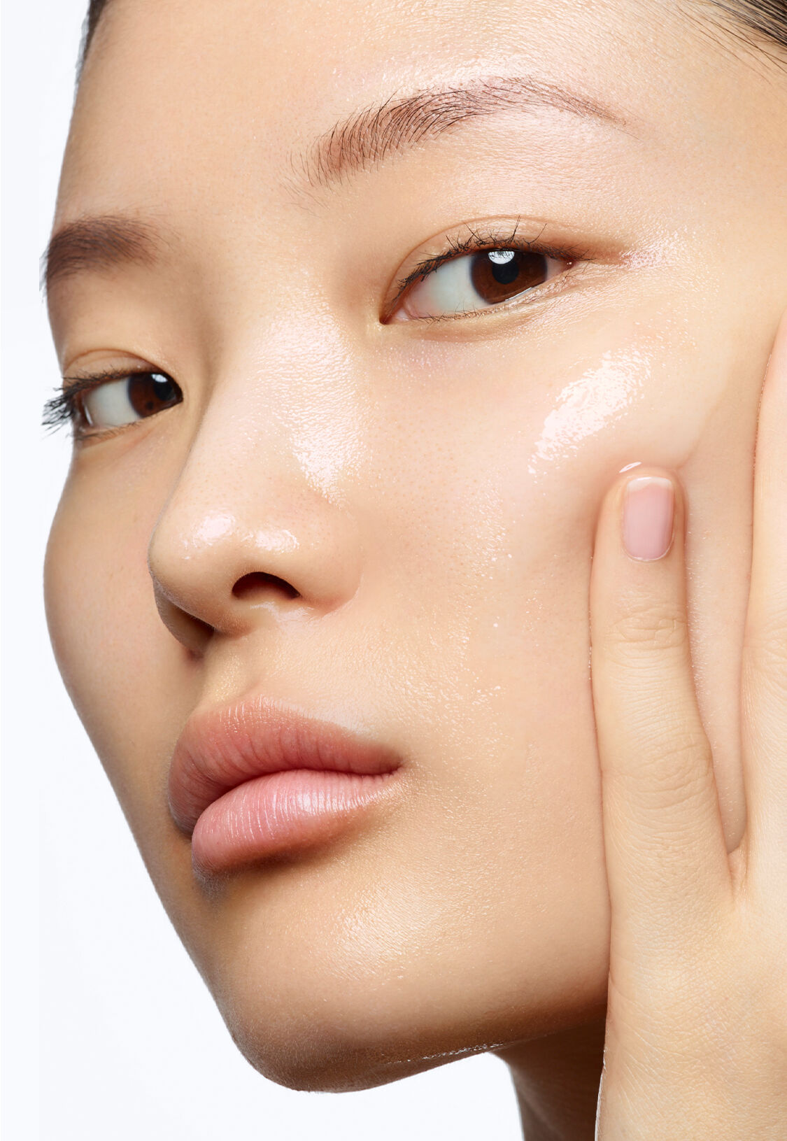 A close-up of a person gently touching their cheek, showcasing clear skin with a natural, healthy glow. The background is plain white.