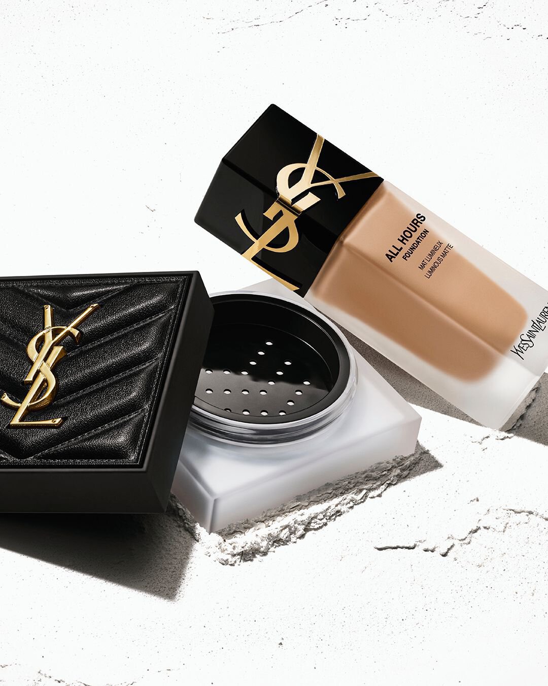 Yves Saint Laurent All Hours Foundation and powder compact displayed against a textured backdrop. The iconic YSL logo is prominently featured on both products.