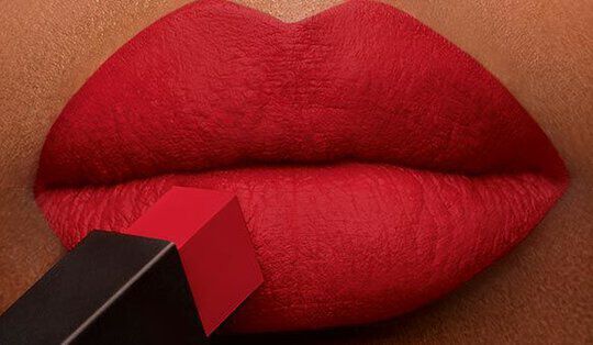 Close-up of a pair of lips coated in vibrant red lipstick, with a lipstick bullet being applied.