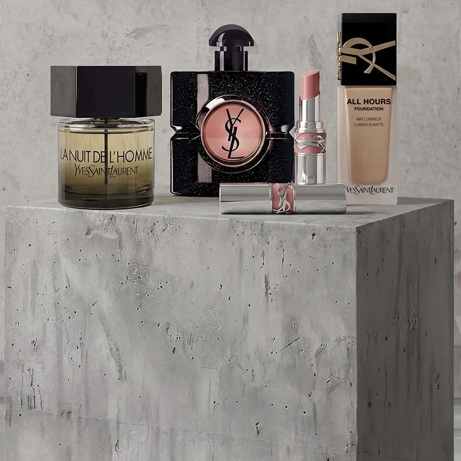 Werbeprasentation von YSL Beaute Make-up-Produkten, darunter Mascara, eine gesteppte Lidschattenpalette und Lippenstifte vor einem Betonhintergrund.