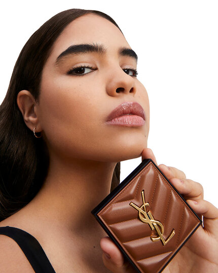 A model poses confidently while holding a brown YSL wallet, showcasing her flawless makeup and sleek hairstyle.
