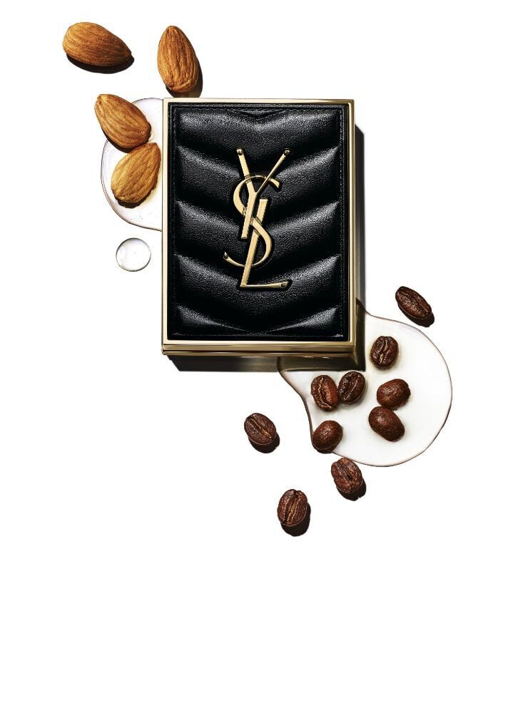 A stylish black purse featuring the YSL logo is surrounded by coffee beans and almonds, set against a gradient background.