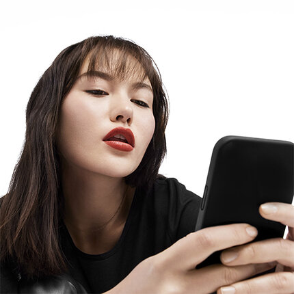 Eine Frau mit langen, dunklen Haaren und rotem Lippenstift schaut auf ihr Smartphone.