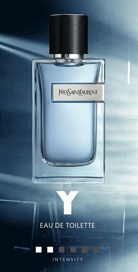 A bottle of Yves Saint Laurent Y Eau de Toilette on a blue background, featuring a sleek design with a dark cap and a silver label. Below the bottle, a color gradient represents different intensities.