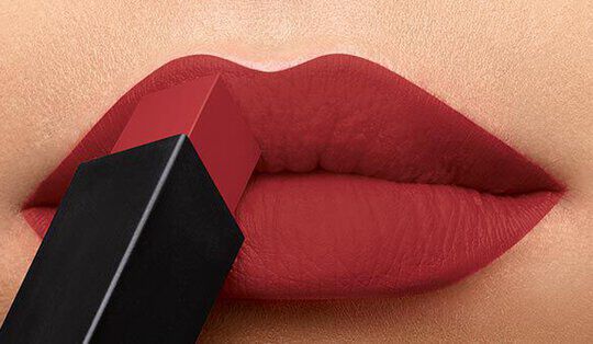 Close-up of lips applying a bold red lipstick with the lipstick tube resting against the mouth.