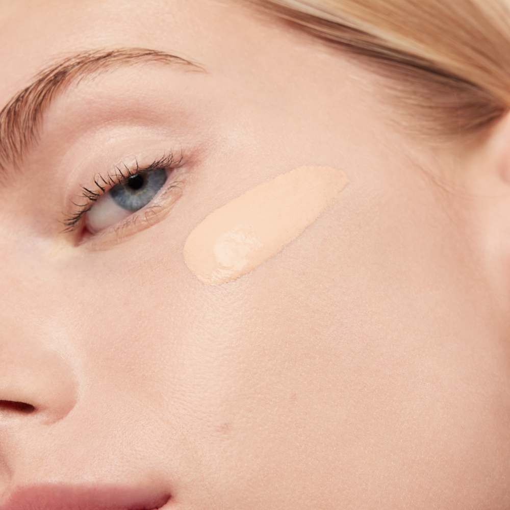 A close-up of a person's face with a light foundation swatched on their cheek, showcasing the skin texture and color.