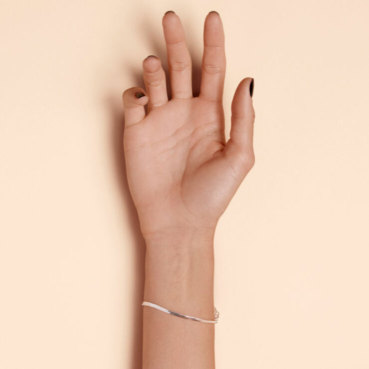 A hand with light skin and neatly manicured nails, resting flat against a pale background, wearing a simple silver bracelet.