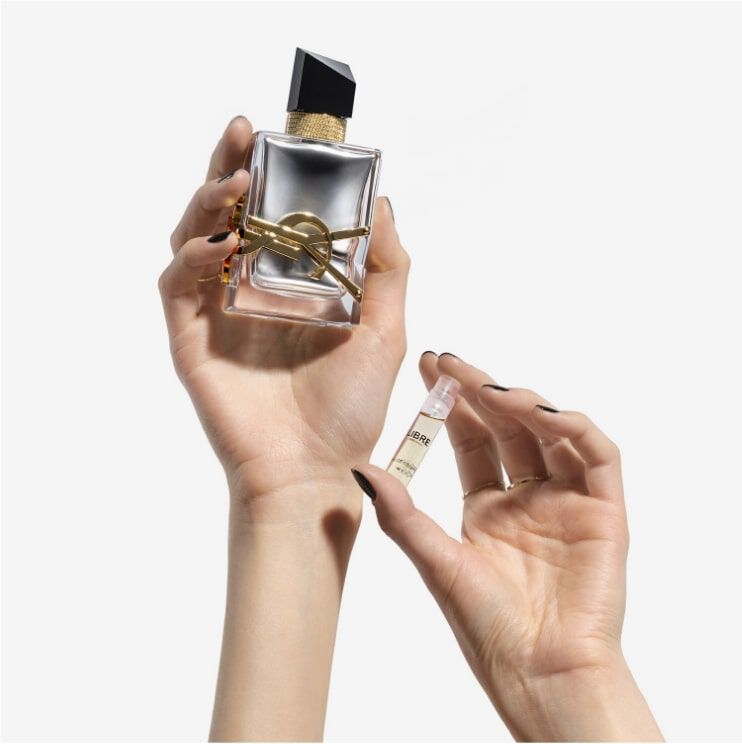 A person holds a stylish perfume bottle in one hand and a small sample vial in the other, showcasing both products.