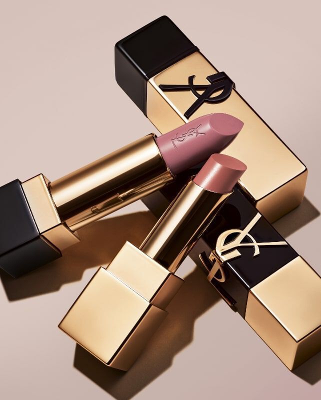 Close-up of luxury lipstick tubes with gold packaging and a soft pink shade, elegantly arranged on a neutral background.