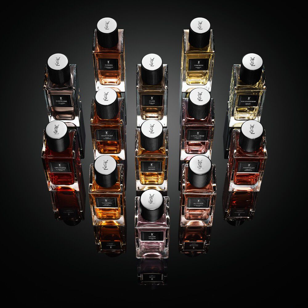 Eine Kollektion von Yves Saint Laurent „Le Vestiaire des Parfums“ Flakons, die rautenformig auf einer reflektierenden schwarzen Oberflache angeordnet sind.