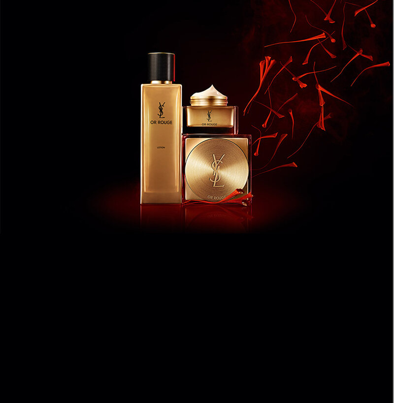 A collection of YSL Or Rouge skincare products, including a lotion and two jars, with elegant designs in gold and red against a dark background, accented by floating red flower petals.