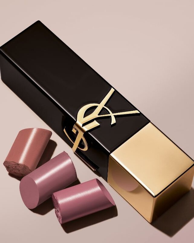 A luxurious makeup package in black and gold, featuring the YSL logo, accompanied by three lipstick bullets in various shades of pink.