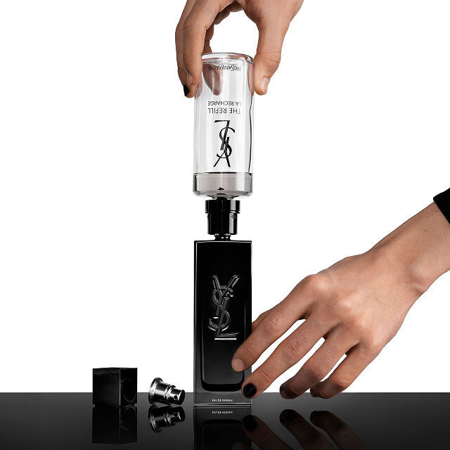 Die Hande einer Person fullen einen schwarzen Yves Saint Laurent (YSL) Parfumflakon mit einer transparenten Nachfullkartusche auf, die „THE REFILL LA RECHARGE“ beschriftet ist.