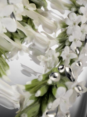 An abstract close-up of delicate white flowers and green foliage, with shiny silver accents, set against a soft gradient background.