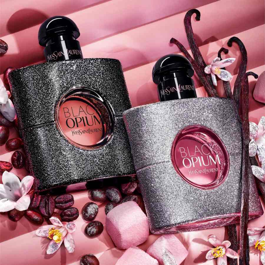 Zwei YSL Black Opium Flakons auf rosa Hintergrund mit Blumen und Kaffeebohnen