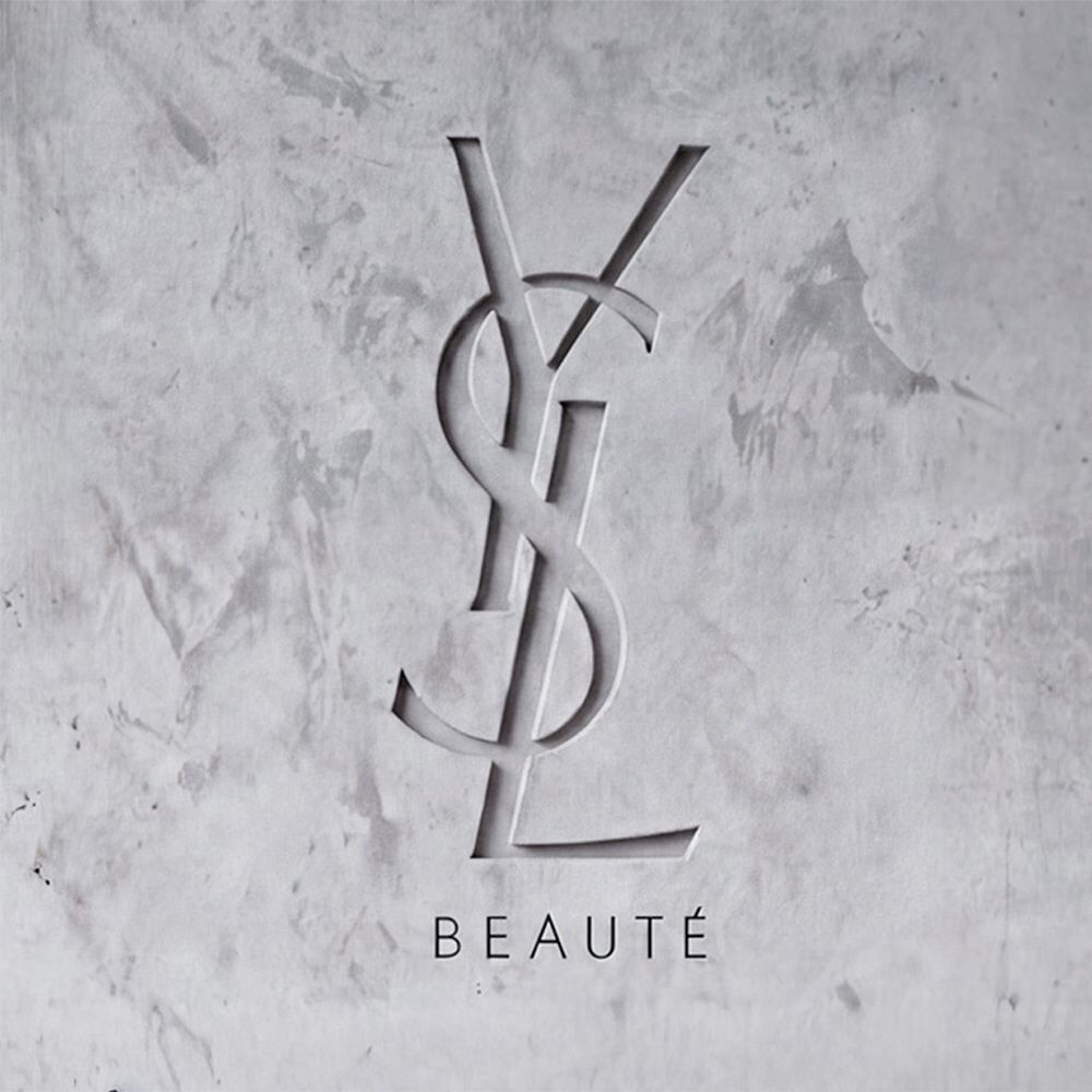In eine strukturierte graue Betonwand graviertes YSL BEAUTE Logo.