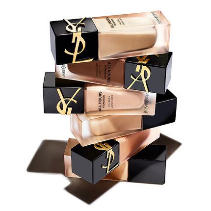 A visually striking arrangement of YSL foundation bottles stacked on top of each other, featuring sleek black and gold packaging against a white background.