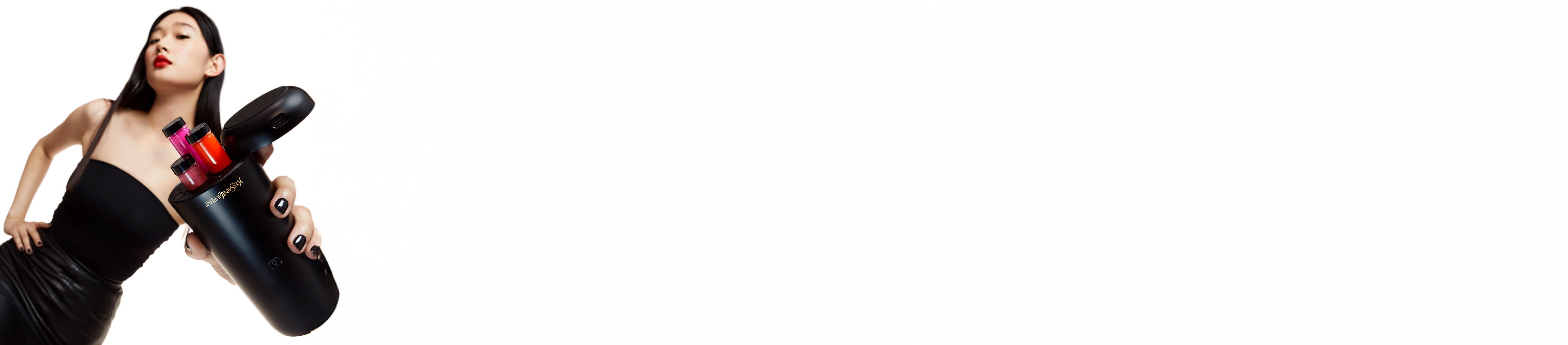 Eine Frau mit rotem Lippenstift halt ein schwarzes Yves Saint Laurent Beauty-Gerat mit farbigen Kosmetikeinsatzen.