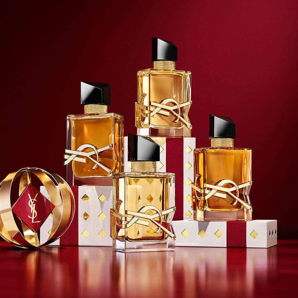 Mehrere Flakons YSL LIBRE, geschichtet uber luxuriosem, goldgemustertem Holiday-Geschenkpapier.