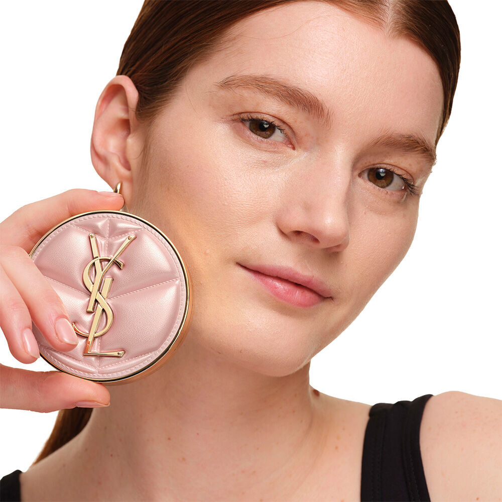 Ein Model mit glatter, strahlender Haut halt das pinke YSL SKIN AFFAIR CUSHION FOUNDATION, um einen naturlich leuchtenden, makellosen Haut-Look zu prasentieren.