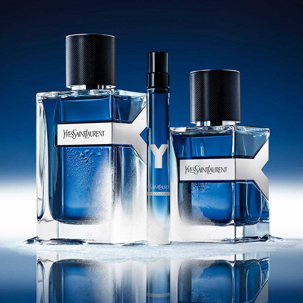 YSL Y Eau de Toilette Intense Iced Cologne Trio: 100ml, 60ml und 10ml Flaschen, mit Wassertropfen bedeckt, auf einer reflektierenden blauen Oberflache.