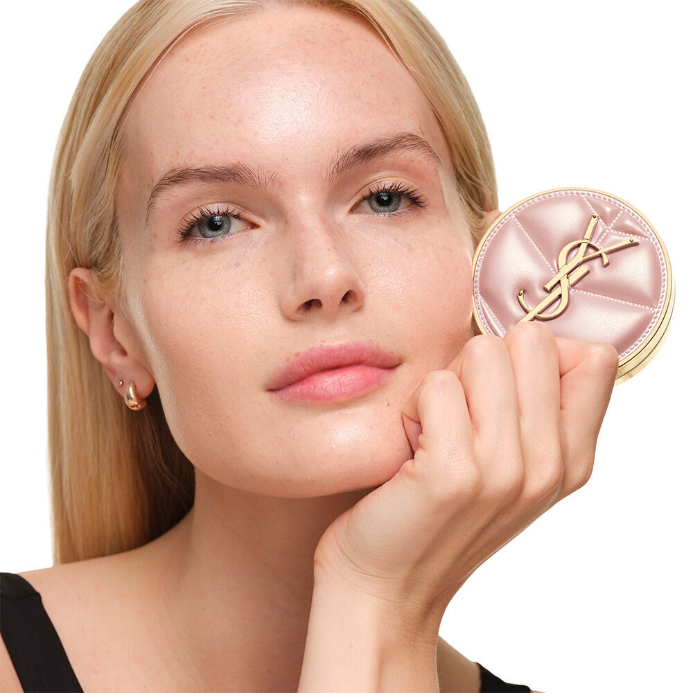 Model mit glatter, strahlender Haut, die das pinkfarbene YSL SKIN AFFAIR CUSHION FOUNDATION halt, um einen naturlich leuchtenden, makellosen Teint zu prasentieren.