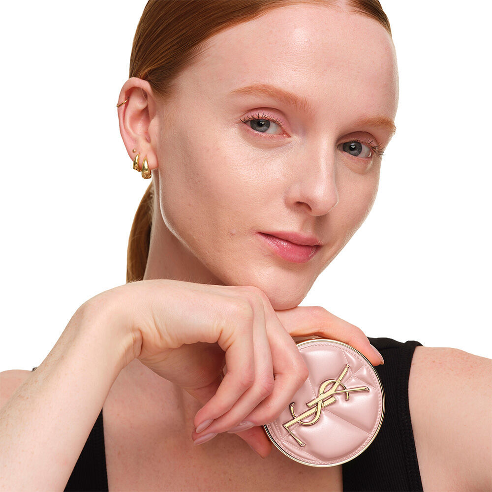Model mit glatter, strahlender Haut halt das pinkfarbene YSL SKIN AFFAIR CUSHION FOUNDATION, um ein naturlich leuchtendes, makelloses Hautbild zu prasentieren.