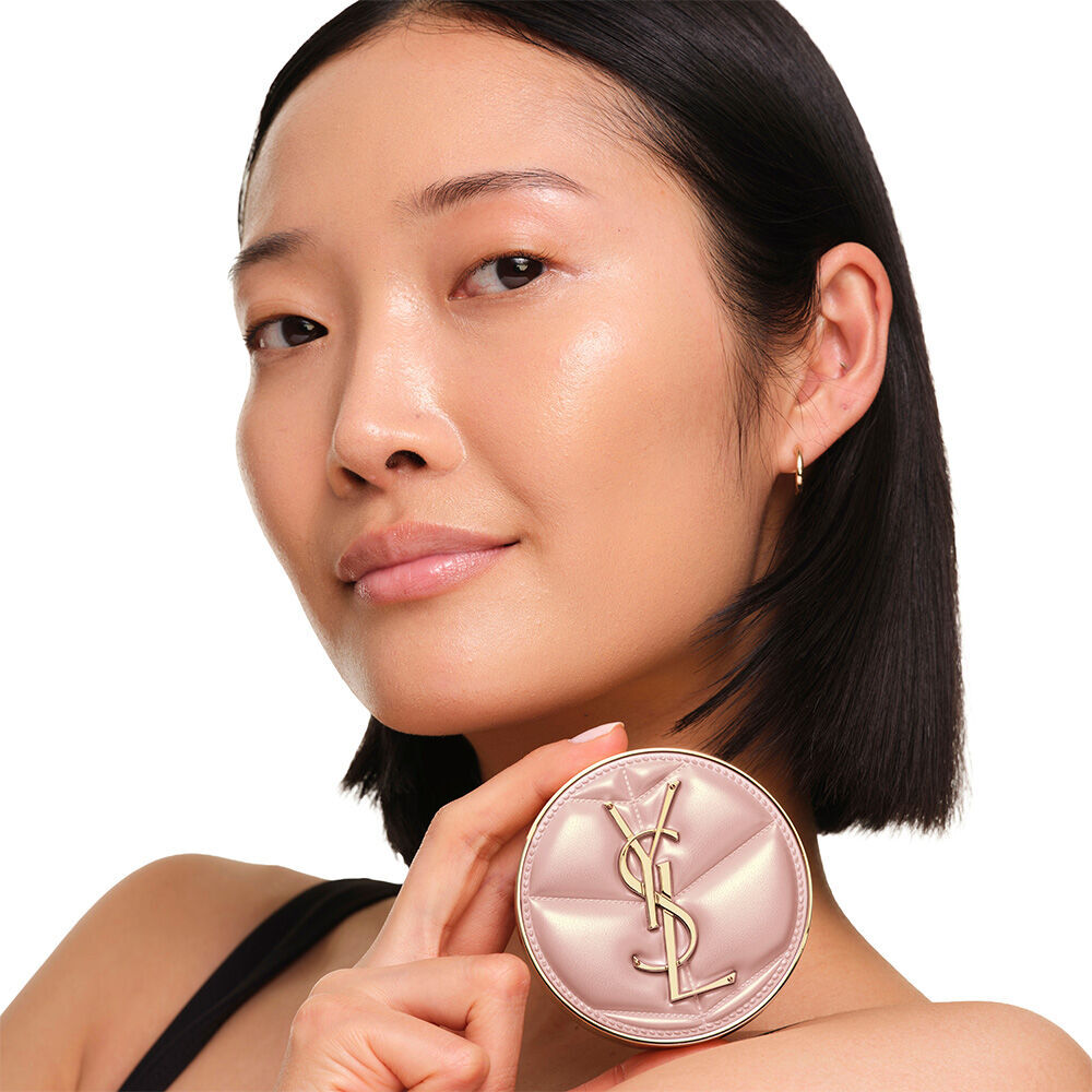 Model mit glatter, strahlender Haut halt das pinke YSL SKIN AFFAIR CUSHION FOUNDATION und prasentiert einen naturlich strahlenden, makellosen Teint.