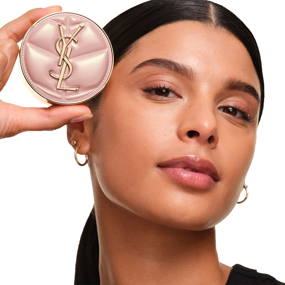 Model mit einem glatten, strahlenden Teint, halt das rosafarbene YSL SKIN AFFAIR CUSHION FOUNDATION und prasentiert einen naturlich leuchtenden, makellosen Haut-Look.