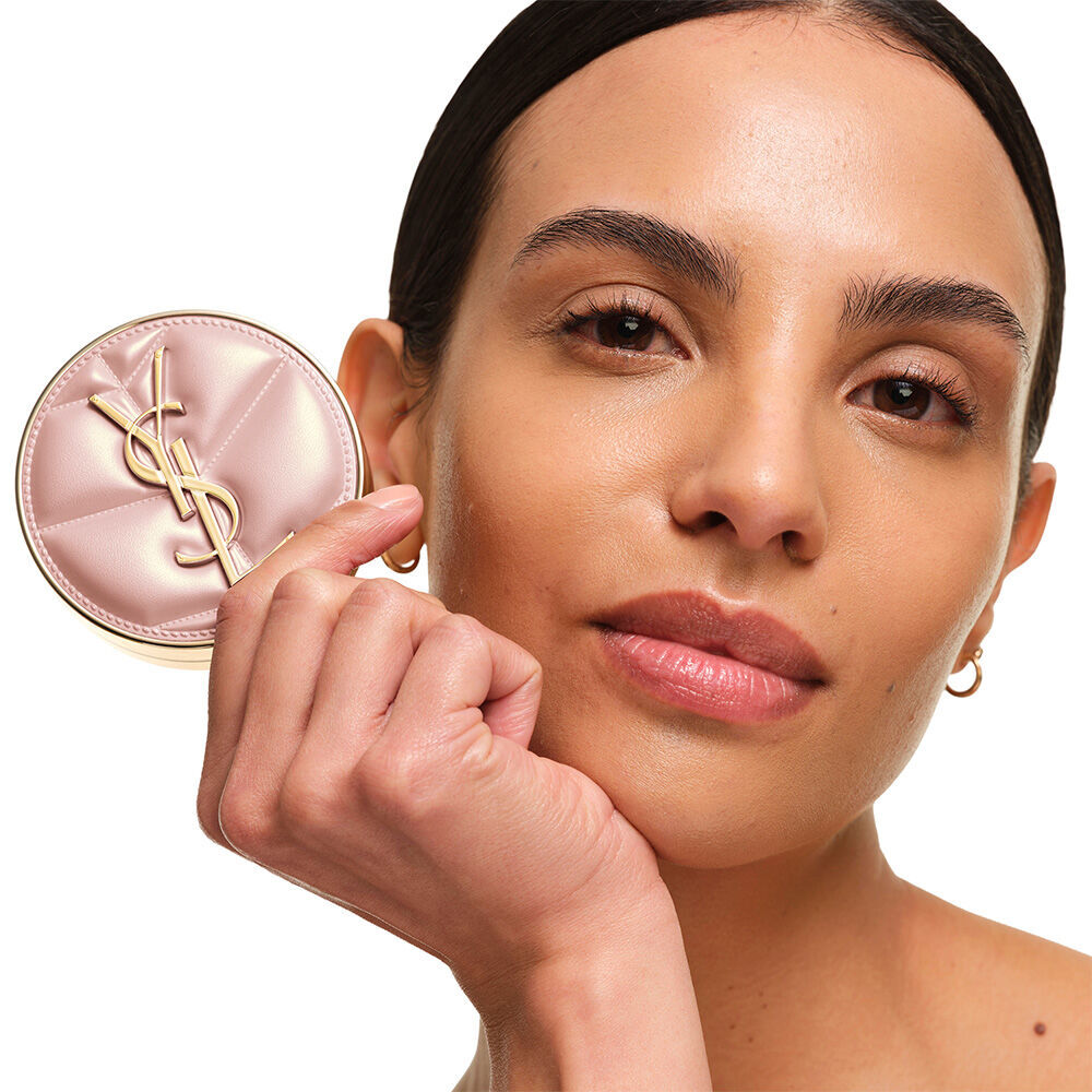 Model mit einem glatten, strahlenden Teint, halt das pinke YSL SKIN AFFAIR CUSHION FOUNDATION und prasentiert eine naturlich leuchtende, makellose Hautoberflache.
