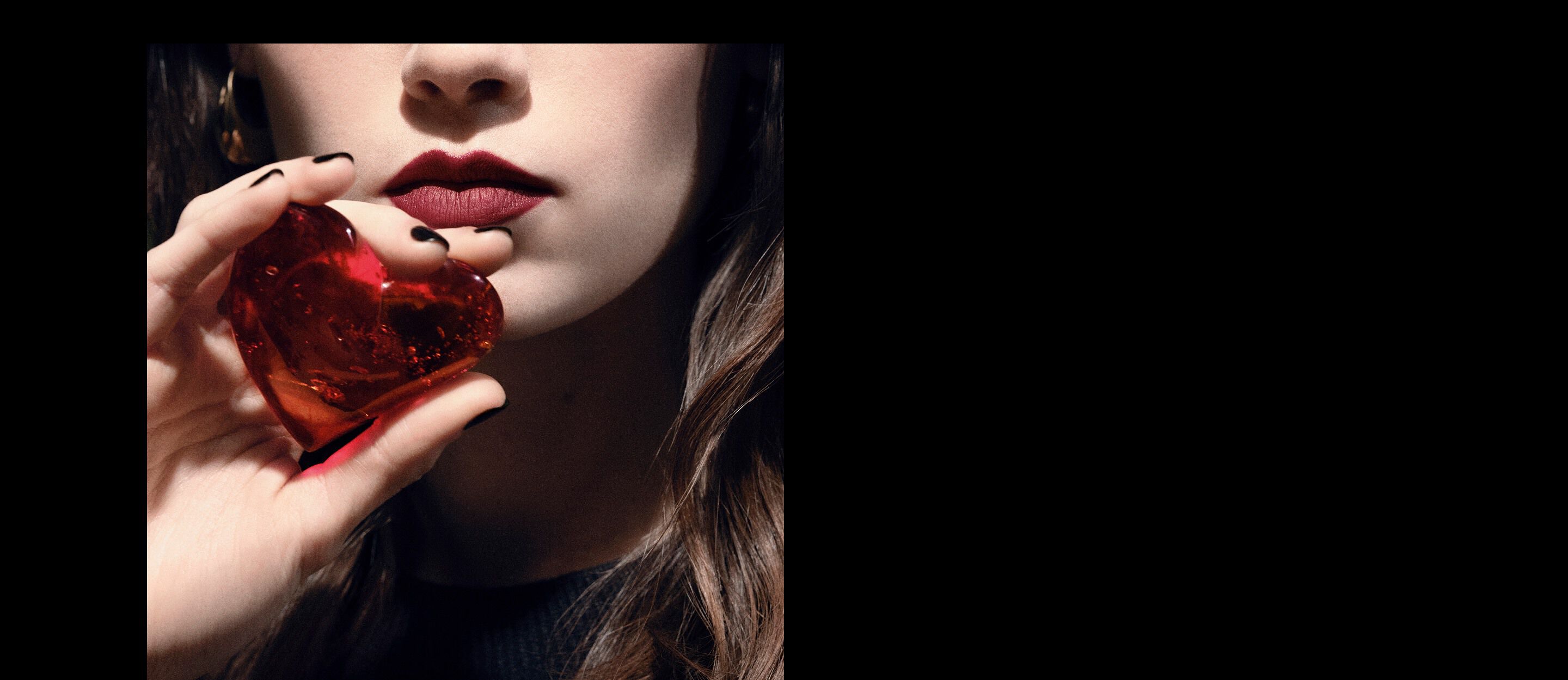 Nahaufnahme der Lippen und Hand eines Models,
das ein durchscheinendes rubinrotes Herzjuwel
für YSL CŒUR Eau de Parfum hält.