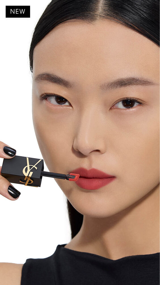 Asiatisches Modell mit hellem Hautton, das einen warmen Rotton von YSL THE INKS BLUR Lip Stain mit dem Applikator aufträgt.