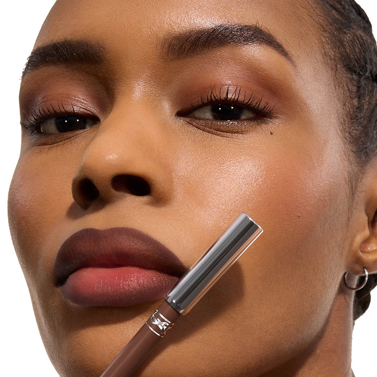 Nahaufnahme eines Models mit braunen Ombré-Lippen, das einen passenden YSL-Lippenkonturenstift hält.