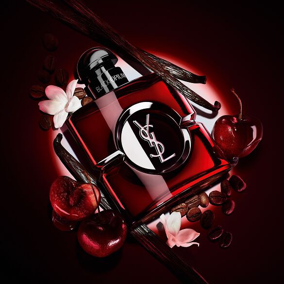 Black Opium Over Red Flakon in tiefrotem Lack, umgeben von frischen roten Kirschen und gerösteten Kaffeebohnen.
