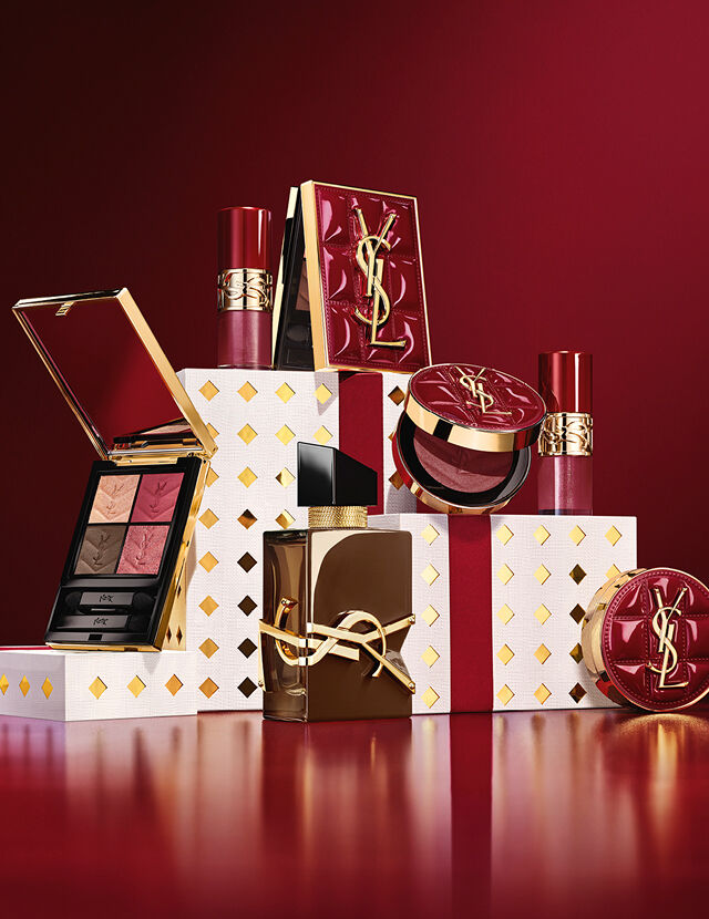 YSL Holiday 2026 Make-up-Kollektion und Duftset auf goldgepunkteten weißen Sockeln in Bordeauxrot.