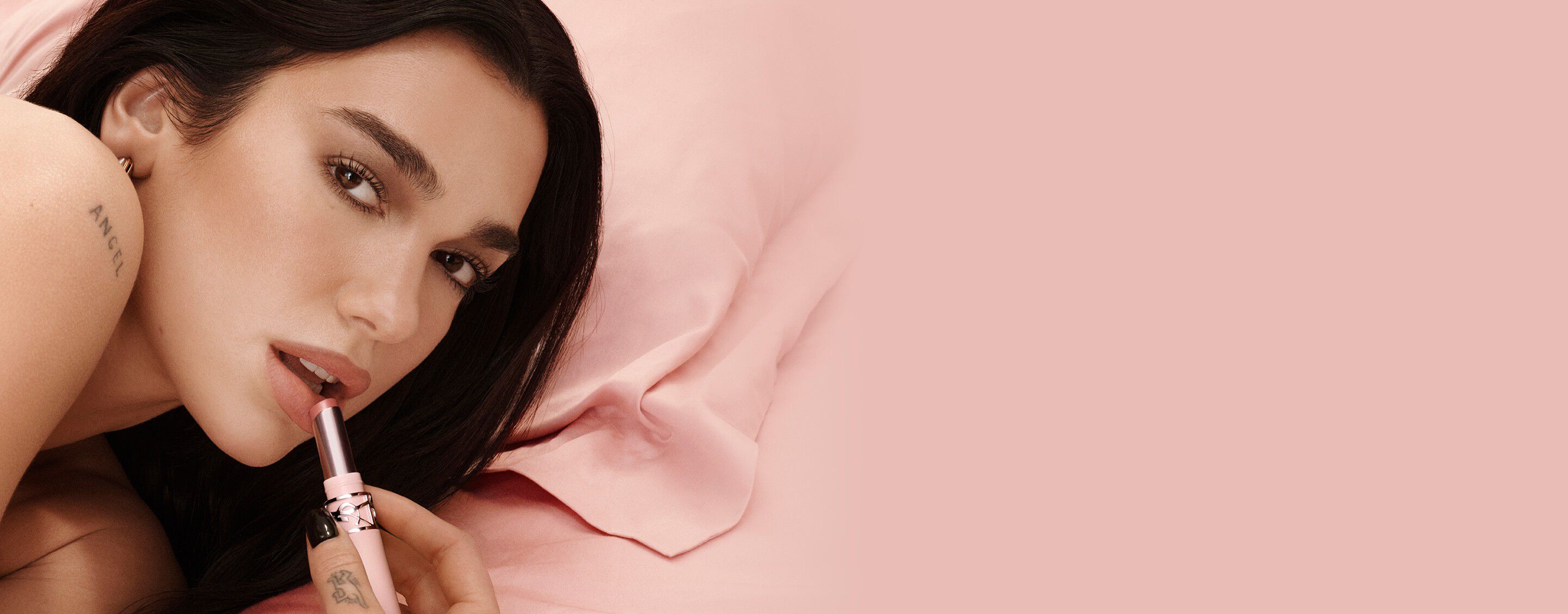 Dua Lipa, YSL Beauty ambassador, applying YSL LOVENUDE Lip Blusher in shade 44, on a soft pink background.