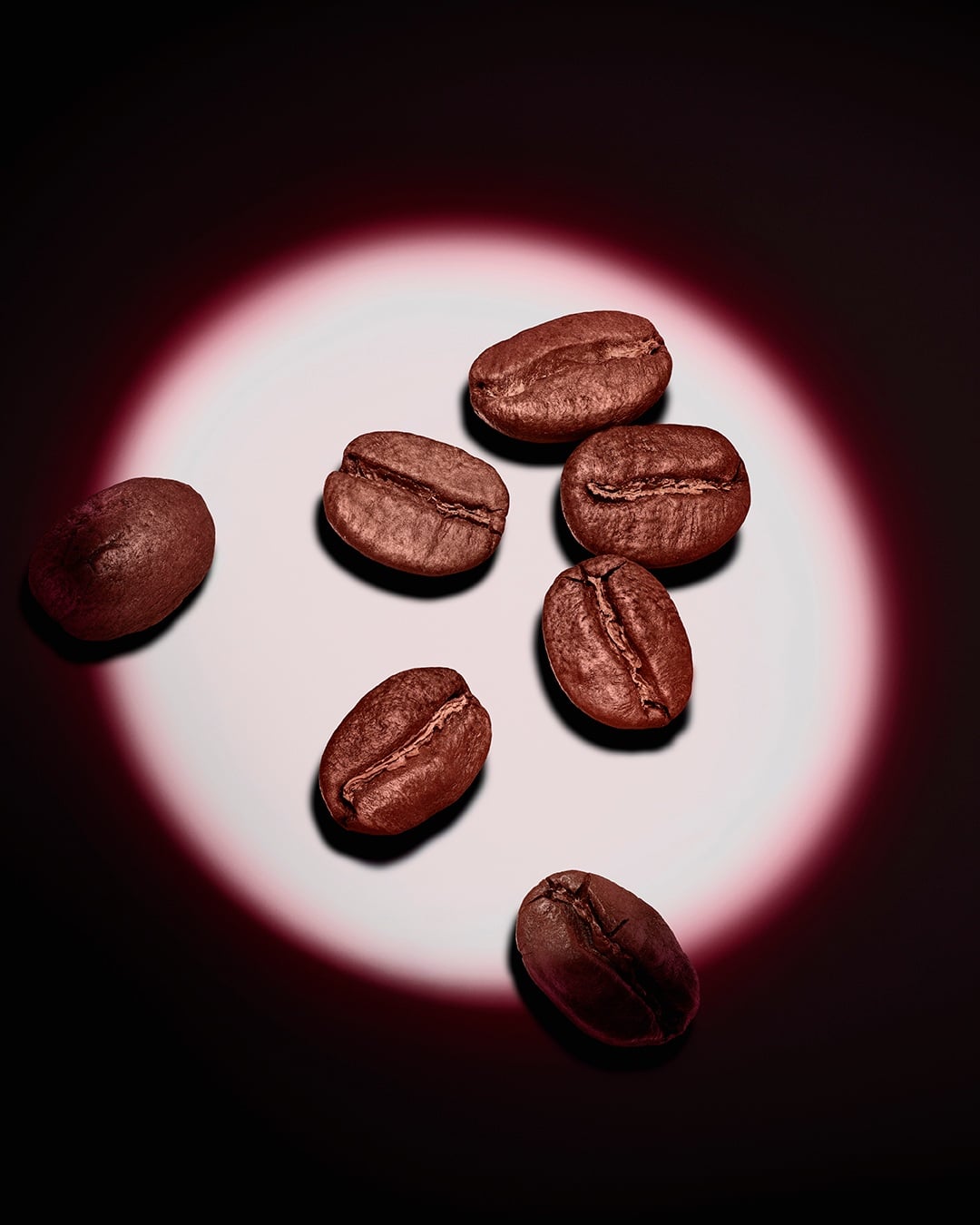 Eine Gruppe gerösteter Kaffeebohnen, akzentuiert durch einen rosafarbenen kreisförmigen Lichtschein auf dunklem Hintergrund.