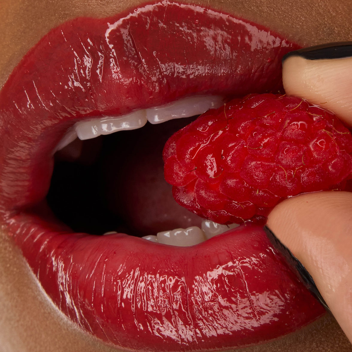 Nahaufnahme der Lippen von Model Zahara, geschminkt mit dem YSL LOVESHINE Lippenstift in der Nuance Berry Crush (Nr. 219), während sie eine frische Himbeere hält.