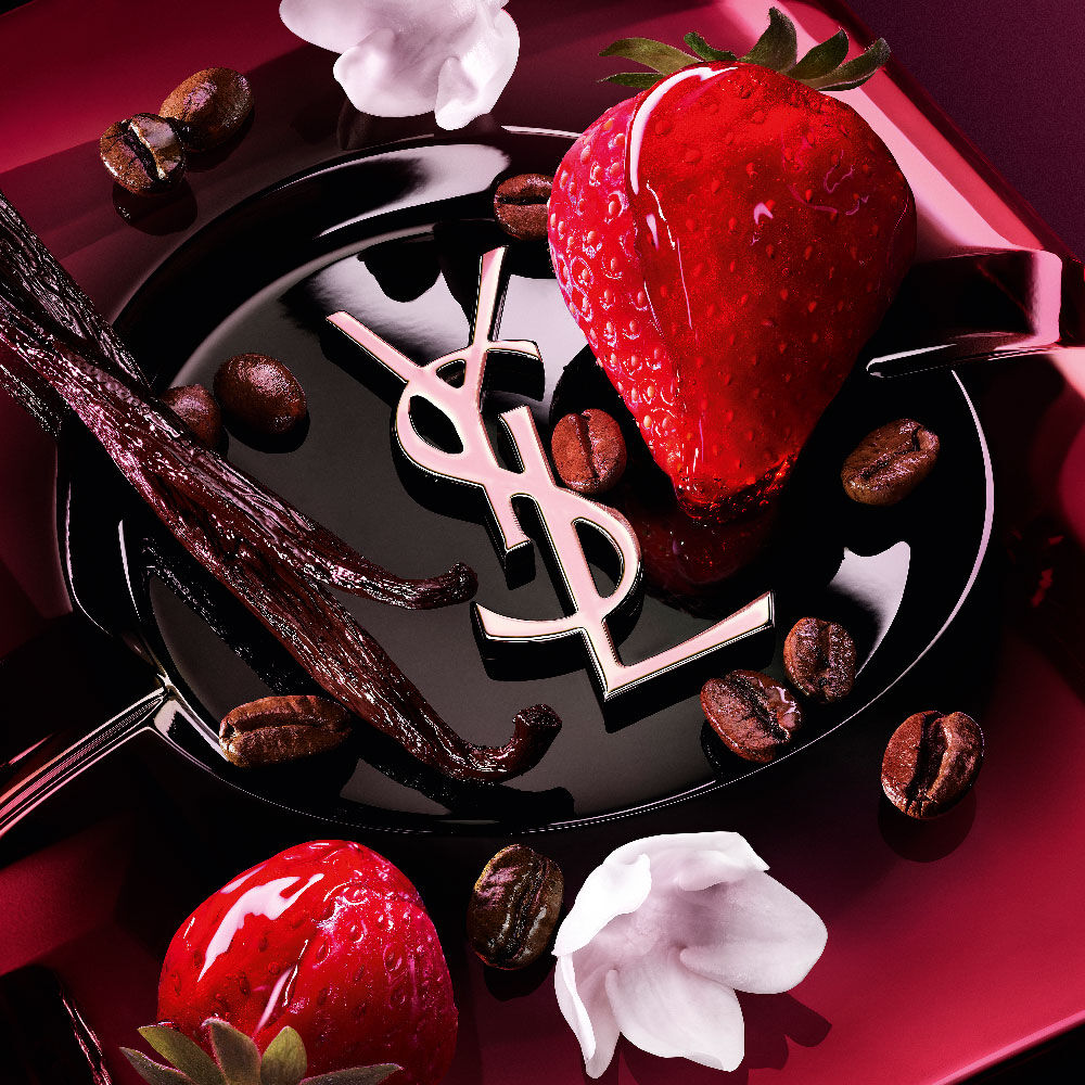 Close-up of fresh strawberries, vanilla pods, jasmine flowers, and roasted
                coffee beans arranged over the Black Opium Eau de Parfum Pink Glaze bottle with the
                iconic YSL cassandre.