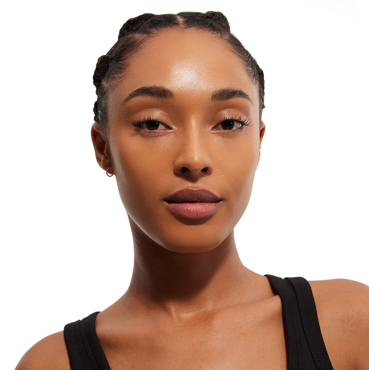 Kopfaufnahme einer Frau mit geflochtenen Haaren und makelloser Haut, die ein schwarzes Oberteil trägt und direkt den Betrachter ansieht, wobei ihr Make-up im Gesicht gezeigt wird.
