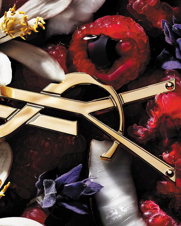 YSL-Logo umgeben von Himbeeren, weißen und violetten Blumen und Kokosnuss.