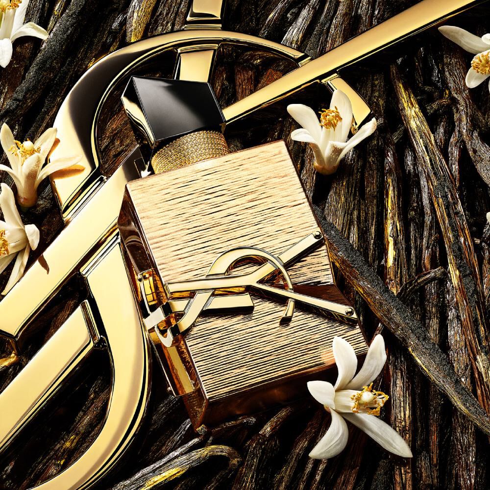 Nahaufnahme des goldenen Libre Vanille Couture Flakons, umgeben von Schlüsselzutaten wie Orangenblüte.