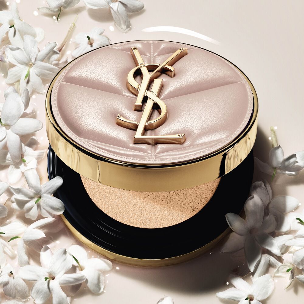 Nahaufnahme des YSL SKIN AFFAIR SOFT GLOW CUSHION in einem Pool aus flüssigem Make-up und Jasminblüten. Strahlendes, sinnliches Finish.